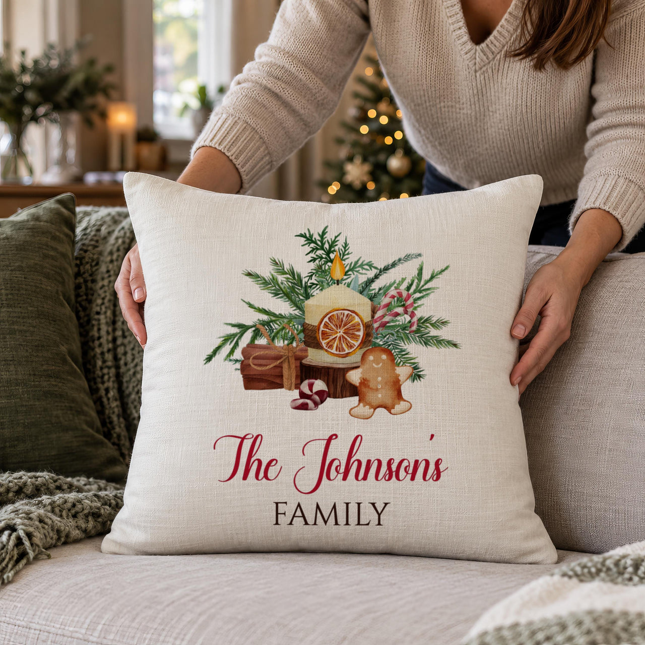 Woman placing a linen cushion with candle, pine and gingerbread artwork and 'The Johnson's FAMILY' - personalised cushion