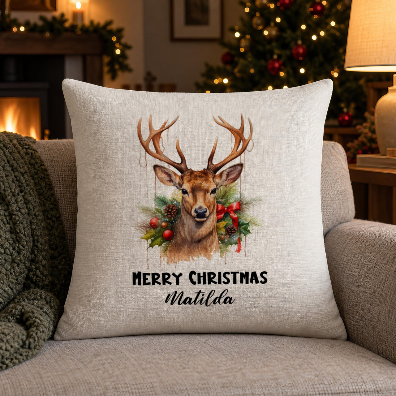Linen-look reindeer wreath cushion 'MERRY CHRISTMAS Matilda' by a lit Christmas tree and fire - personalised cushion