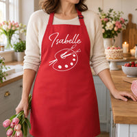Red apron with white 'Isabelle' and paint palette design, holding pink tulips - personalised apron