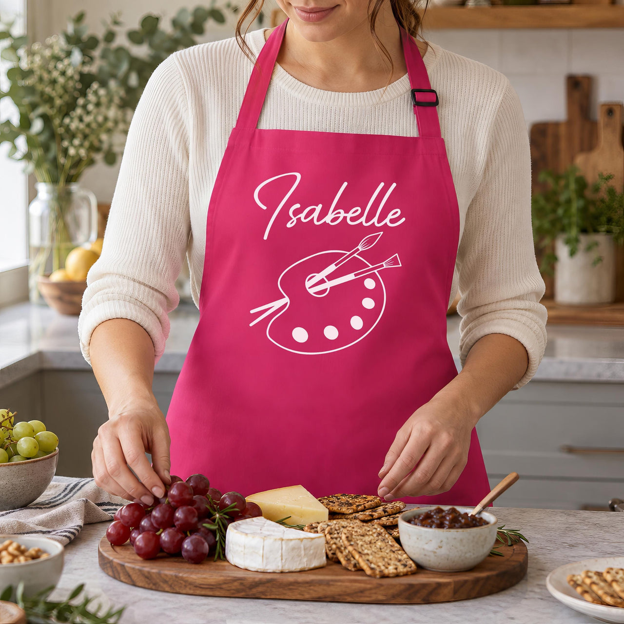 Pink apron with 'Isabelle' and palette, worn while arranging a cheese board - personalised apron