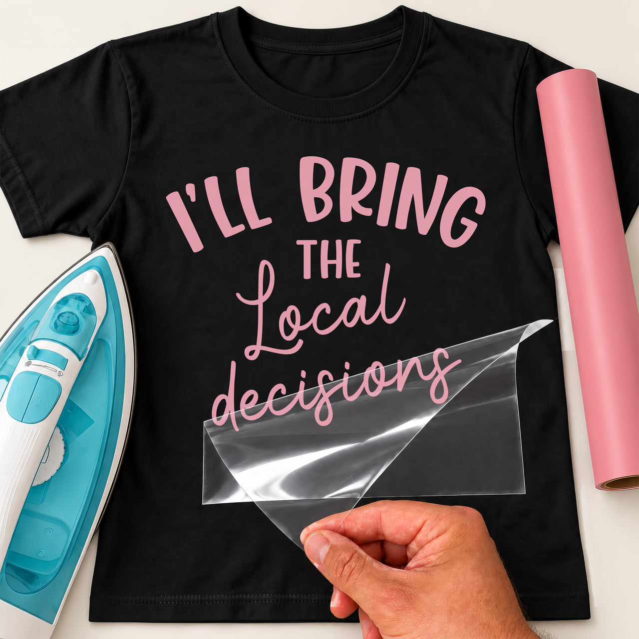 Black T-shirt with pink 'I'LL BRING THE Local decisions' lettering, carrier film being peeled off - iron-on vinyl transfer