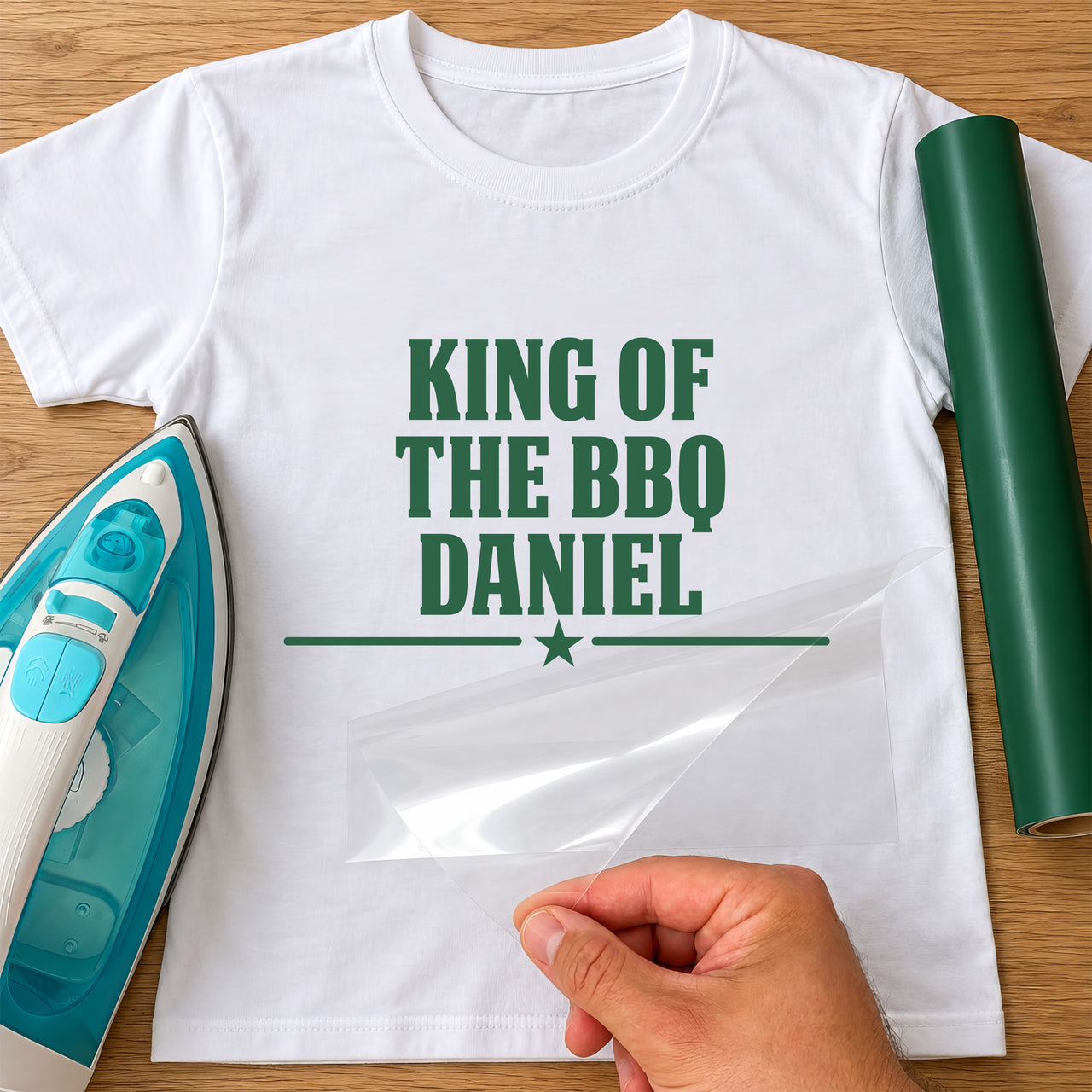 Mockup: white T-shirt with green "KING OF THE BBQ DANIEL" and a star divider, iron and green vinyl roll