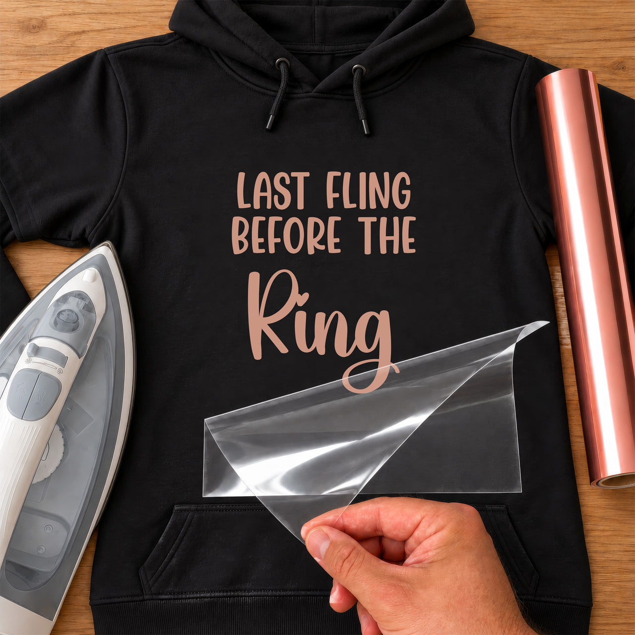 Last Fling iron-on transfer: rose gold LAST FLING BEFORE THE Ring on a black hoodie, film being peeled