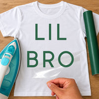 White T-shirt with green iron-on vinyl 'LIL BRO' in large capitals, iron and vinyl roll beside
