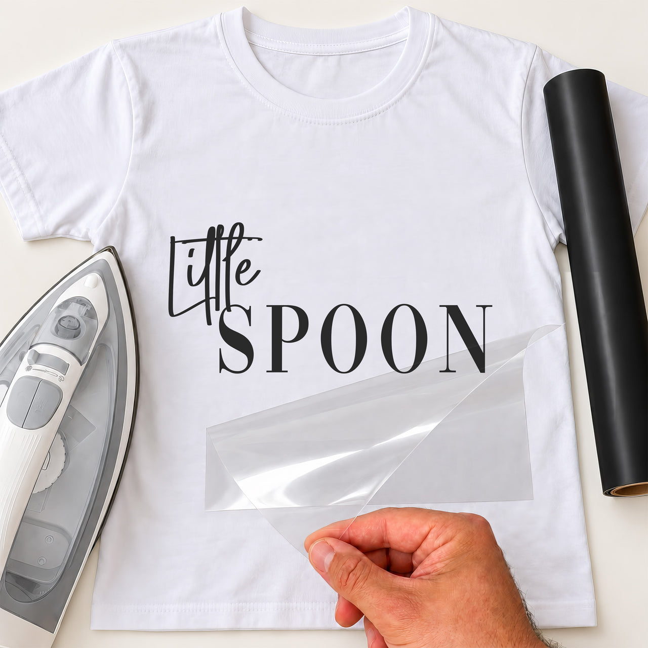 White T-shirt with black 'Little SPOON' lettering, script and serif, carrier film being peeled off - iron-on vinyl transfer