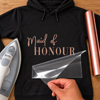 Black hoodie with rose gold script 'Maid of' and serif 'HONOUR' iron-on transfer, iron and vinyl roll