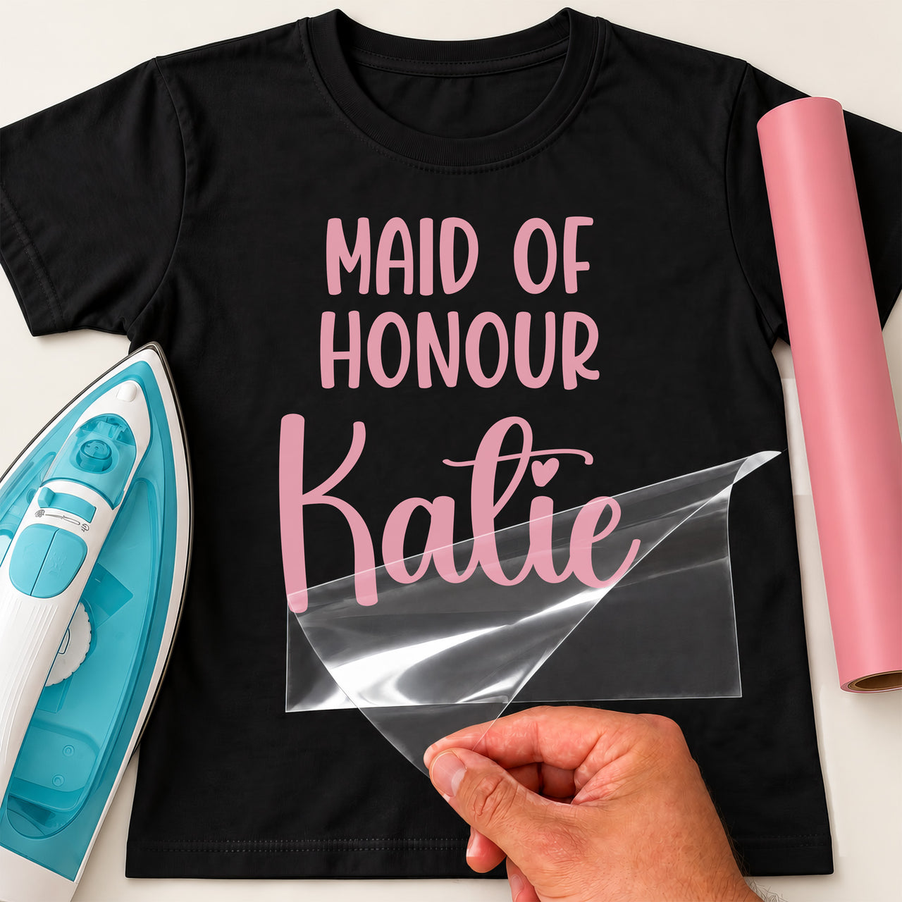 Black T-shirt with pink 'MAID OF HONOUR' and script 'Katie', personalised wedding iron-on transfer being peeled