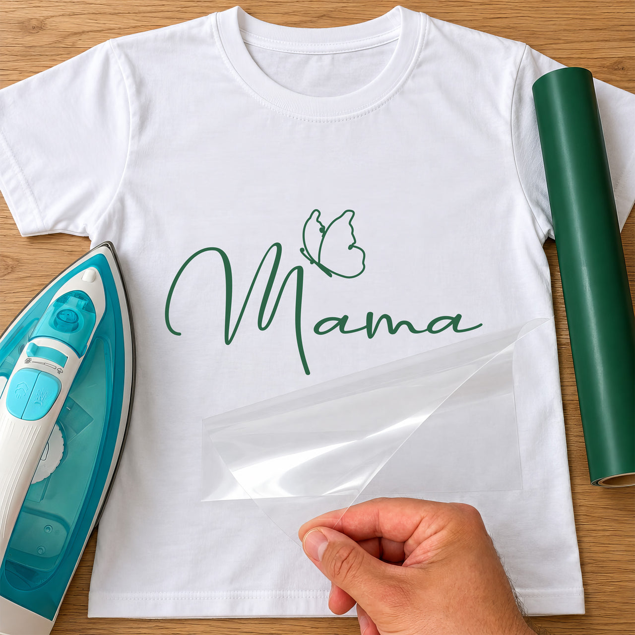 White T-shirt with dark green script 'Mama' and a line-art butterfly, iron-on vinyl transfer being peeled