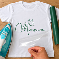 White T-shirt with dark green script 'Mama' and a line-art butterfly, iron-on vinyl transfer being peeled