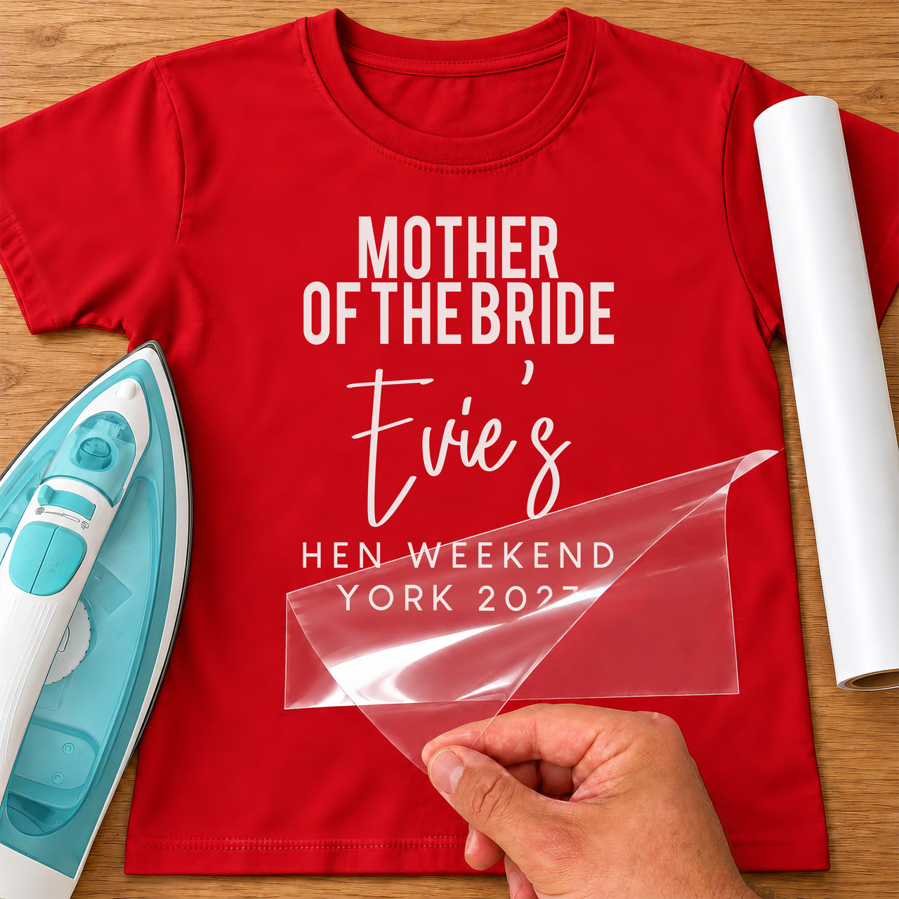 Red T-shirt mockup with white 'MOTHER OF THE BRIDE', script 'Evie's', 'HEN WEEKEND YORK 2027', film being peeled