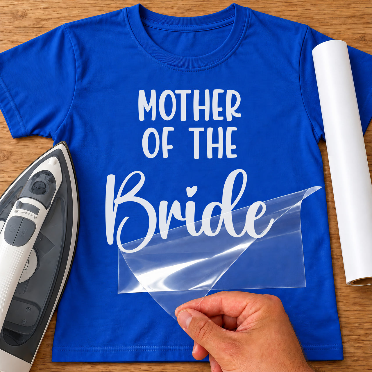 Blue T-shirt with white Mother of the Bride lettering transfer, film being peeled off beside an iron