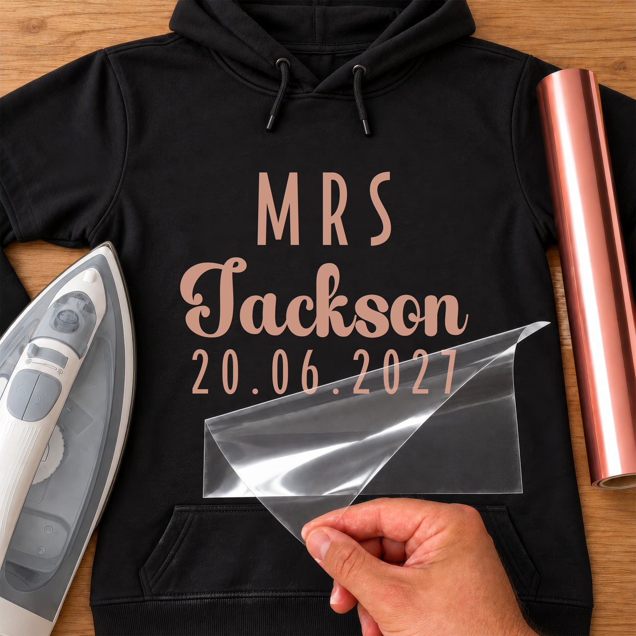 Black hoodie with rose gold 'MRS', a script surname and '20.06.2027', personalised wedding iron-on transfer