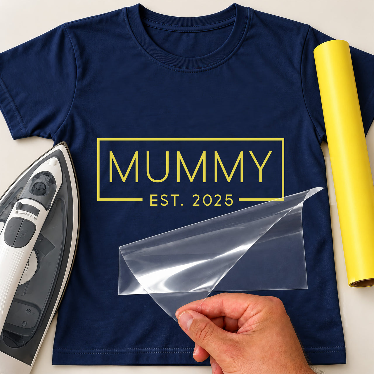 Mockup: navy T-shirt with yellow "MUMMY" inside a thin rectangle frame and "EST. 2025" set into its lower edge