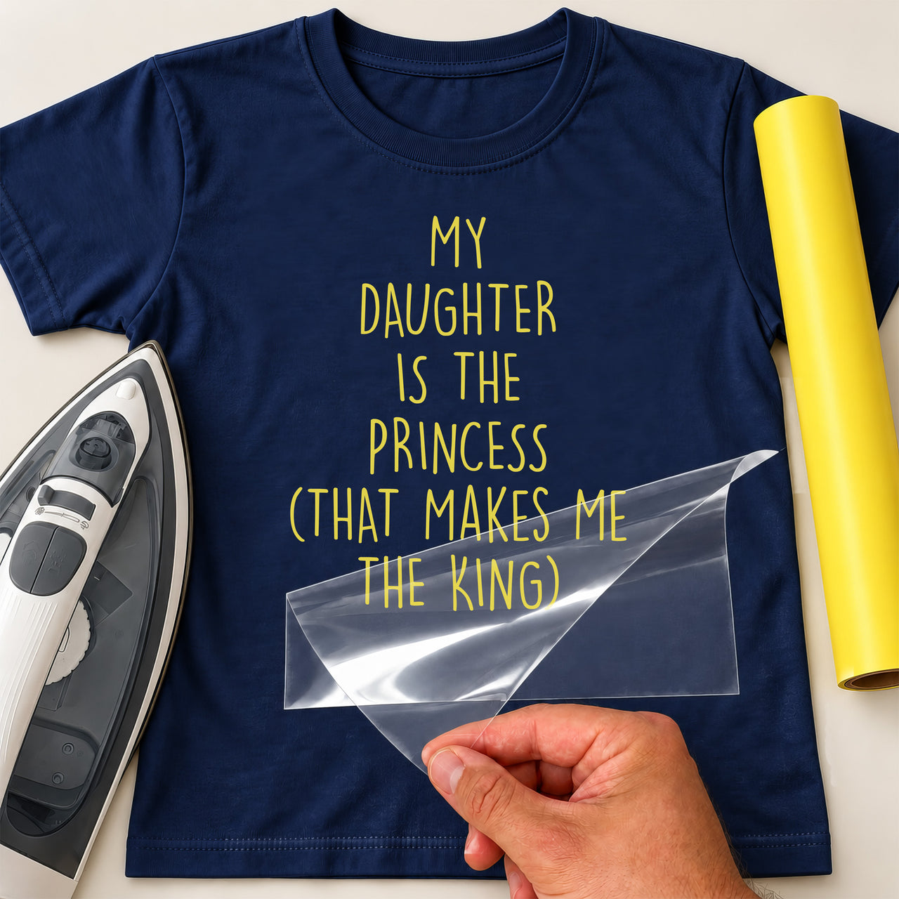 Dad slogan iron-on transfer: yellow MY DAUGHTER IS THE PRINCESS (THAT MAKES ME THE KING) on a navy T-shirt, film being peeled