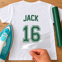 White T-shirt back with green 'JACK' and varsity number '16' iron-on transfer, film peeled away beside a green vinyl roll