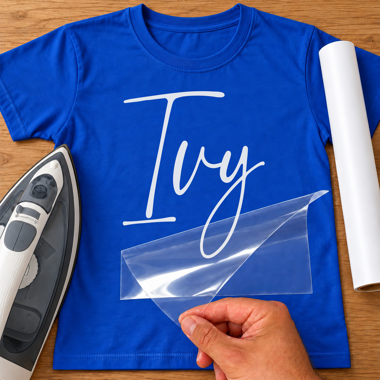 Baby Bodysuit Name iron-on transfer: white script Ivy, shown on a blue T-shirt, film being peeled