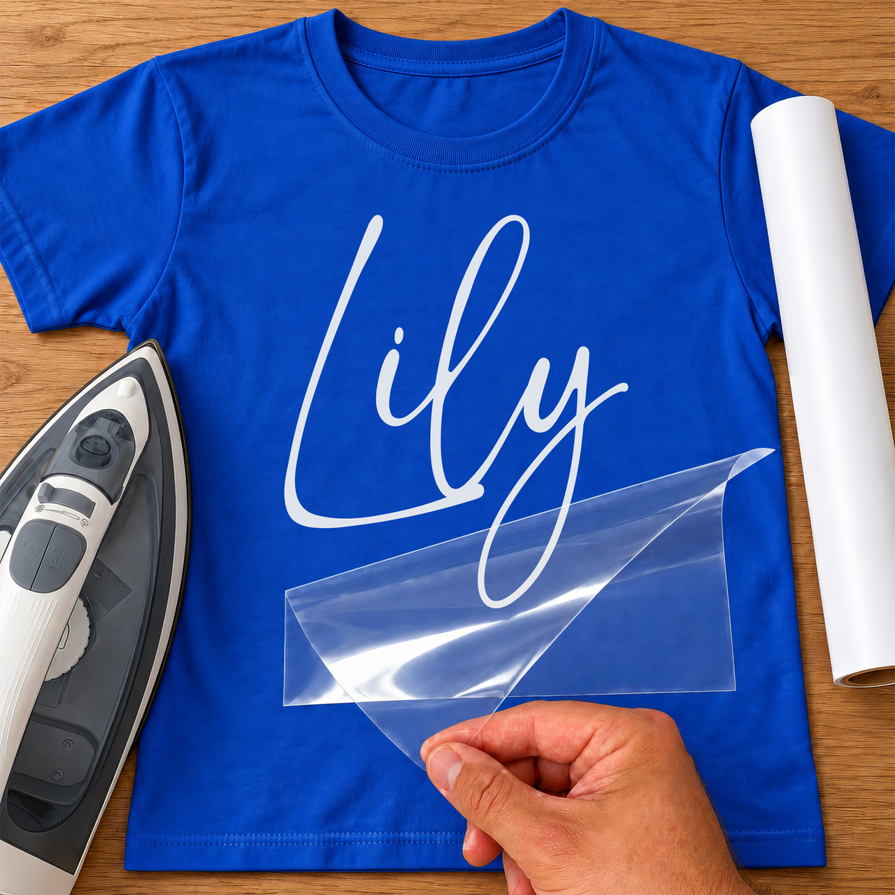 Personalised Ballet Name iron-on transfer: white script Lily on a blue T-shirt, film being peeled