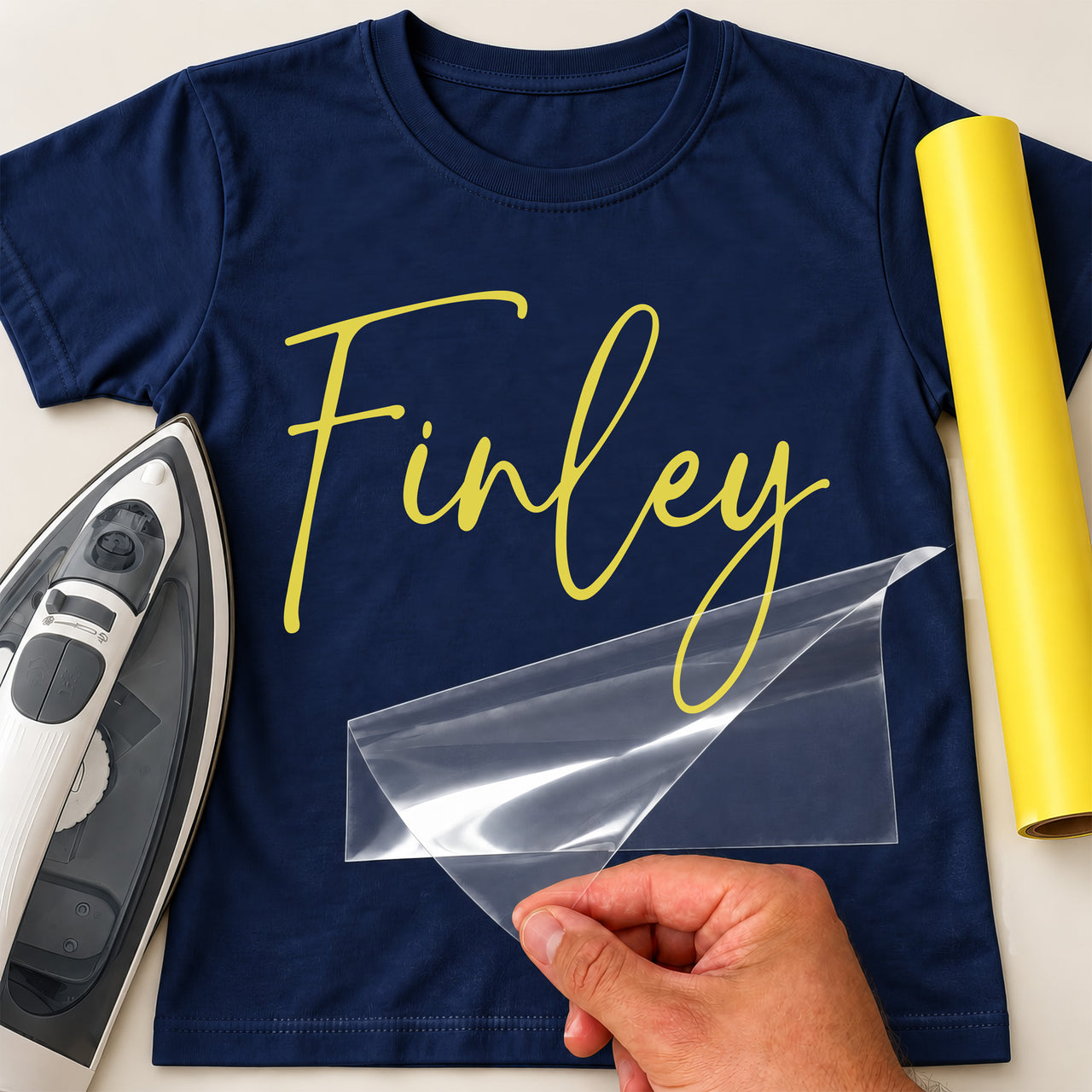 Book Bag and PE Bag Name iron-on transfer: yellow script Finley, shown on a navy T-shirt, film being peeled