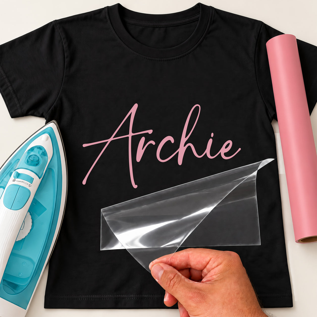 Personalised Carp Angler Name iron-on transfer: pink script Archie on a black T-shirt, film being peeled