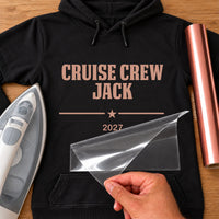 Cruise Crew iron-on transfer: rose gold CRUISE CREW JACK 2027 on a black hoodie, film being peeled