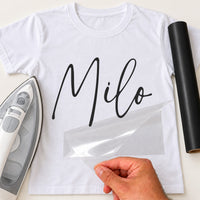 Dog Bandana Name iron-on transfer: black script Milo, shown on a white T-shirt, film being peeled