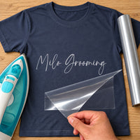 Dog Groomer Name iron-on transfer: silver script Milo Grooming on a navy T-shirt, film being peeled