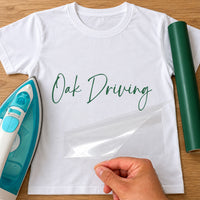 Driving Instructor Name iron-on transfer: green script Oak Driving on a white T-shirt, film being peeled