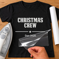 Family Christmas Matching iron-on transfer: white CHRISTMAS CREW Dan 2026 on a black T-shirt, film being peeled