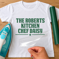 Family kitchen chef iron-on transfer: green THE ROBERTS KITCHEN CHEF DAISY with a star on a white T-shirt, film being peeled