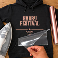 Festival Name iron-on transfer: rose gold HARRY FESTIVAL CREW 2027 on a black hoodie, film being peeled
