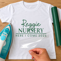 First Day of Nursery iron-on transfer: green Reggie NURSERY HERE I COME 2026 on a white T-shirt, film being peeled