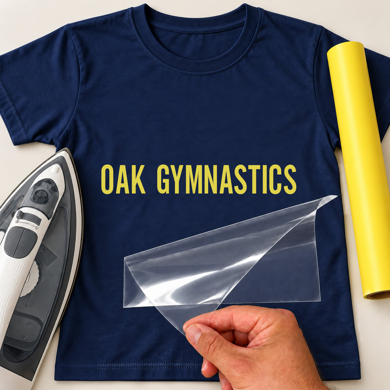 Gymnastics Club Name iron-on transfer: yellow OAK GYMNASTICS on a navy T-shirt, film being peeled