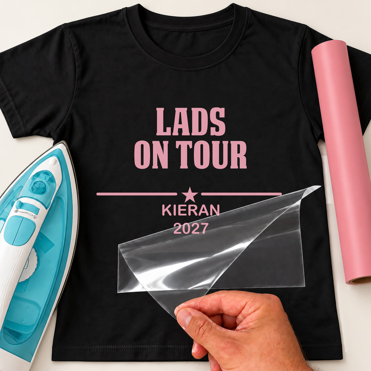 Lads Holiday iron-on transfer: pink LADS ON TOUR KIERAN 2027 on a black T-shirt, film being peeled