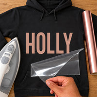 Lash Tech Name iron-on transfer: rose gold HOLLY on a black hoodie, film being peeled