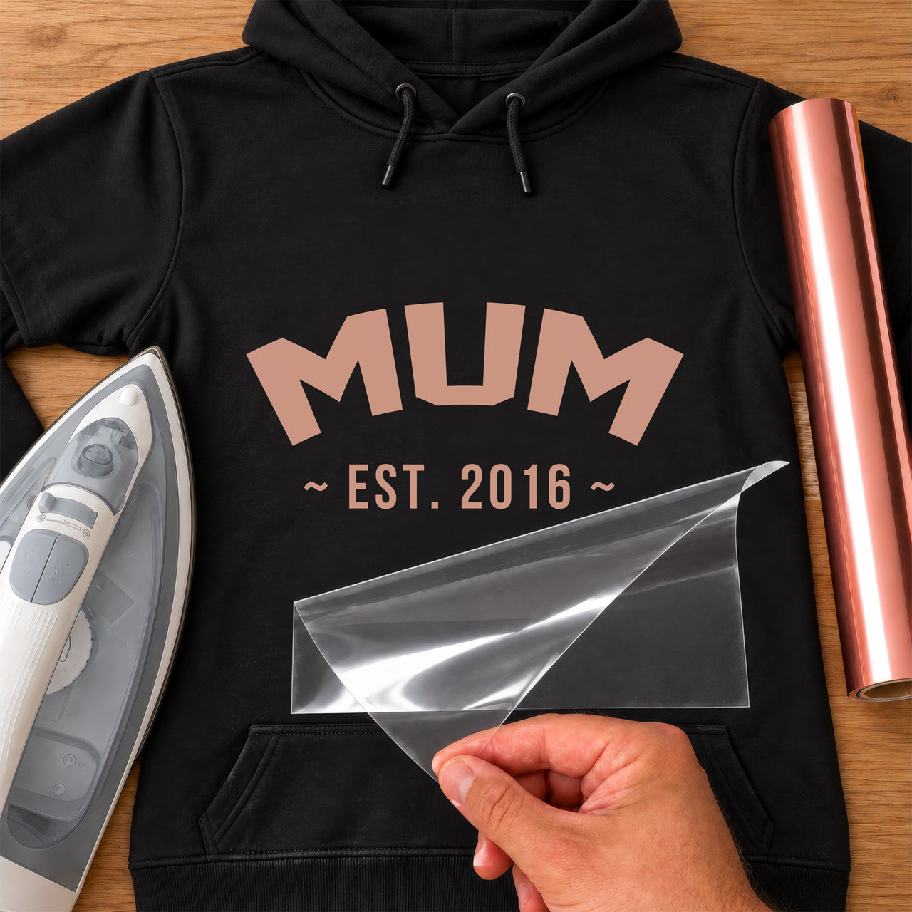 Mum Est. Year iron-on transfer: rose gold MUM EST. 2016 on a black hoodie, film being peeled