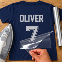 Referee Kit Name Number iron-on transfer: silver OLIVER 7 on a navy T-shirt, film being peeled