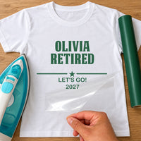 Retirement Text iron-on transfer: green OLIVIA RETIRED, LET'S GO! 2027 on a white T-shirt, film being peeled