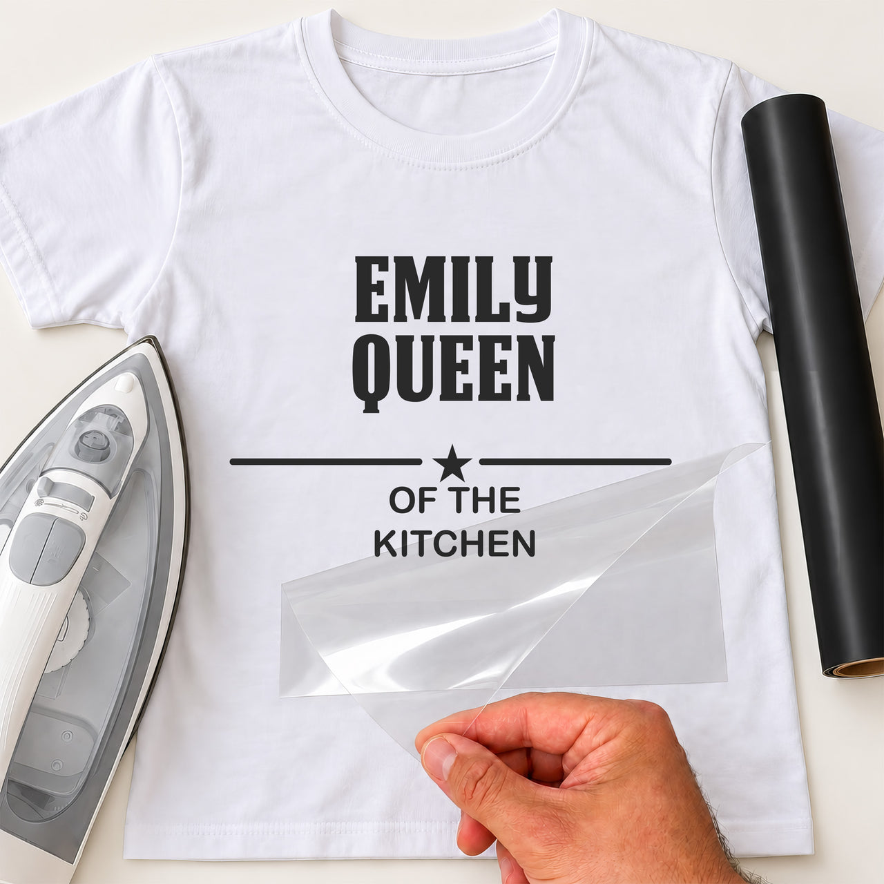 Queen of the Kitchen iron-on transfer: black EMILY QUEEN OF THE KITCHEN with a star on a white T-shirt, film being peeled