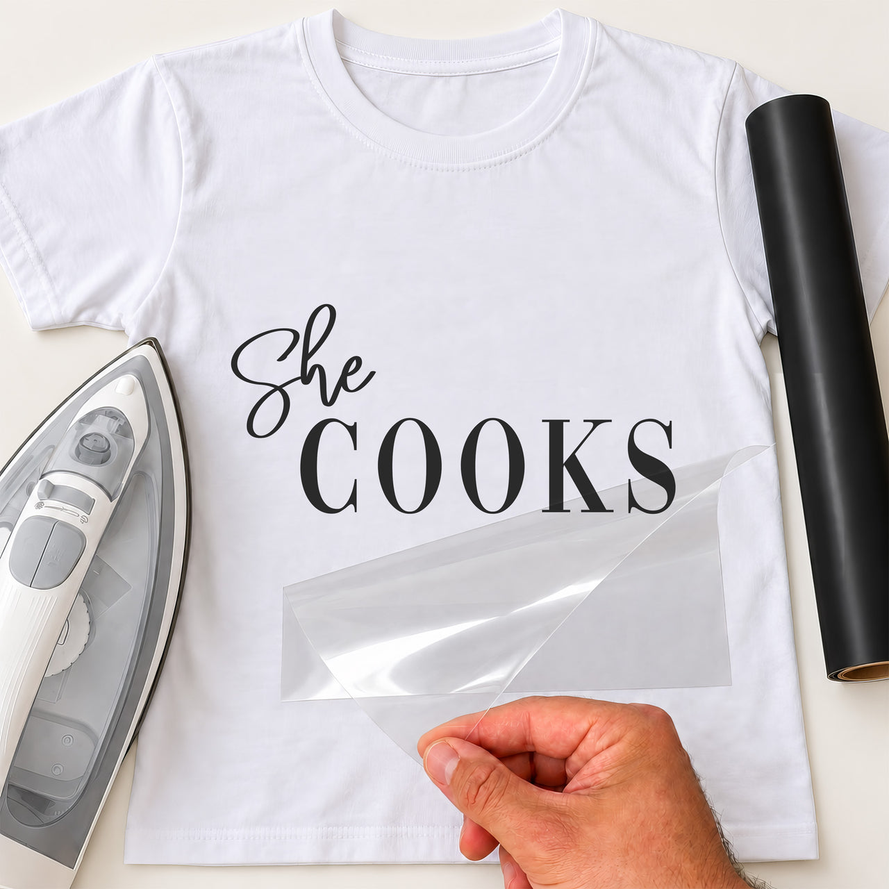 She Cooks iron-on transfer: black She COOKS on a white T-shirt, film being peeled
