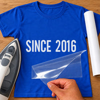 Royal blue T-shirt with white iron-on vinyl reading 'SINCE 2016' being peeled, iron and white vinyl roll beside