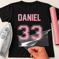 Stag Do Football Shirt Name Number iron-on transfer: pink DANIEL 33 on a black T-shirt, film being peeled