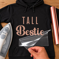 Black hoodie with rose gold iron-on vinyl 'TALL Bestie', iron and vinyl roll beside