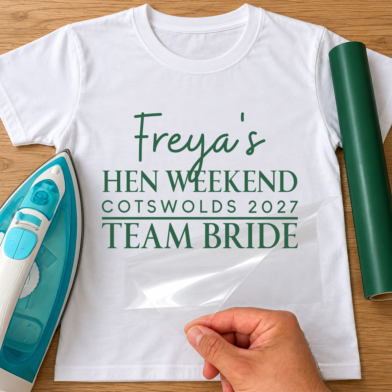 White tee with green 'Freya's Hen Weekend, Cotswolds 2027, Team Bride' in iron-on vinyl, film peeled back
