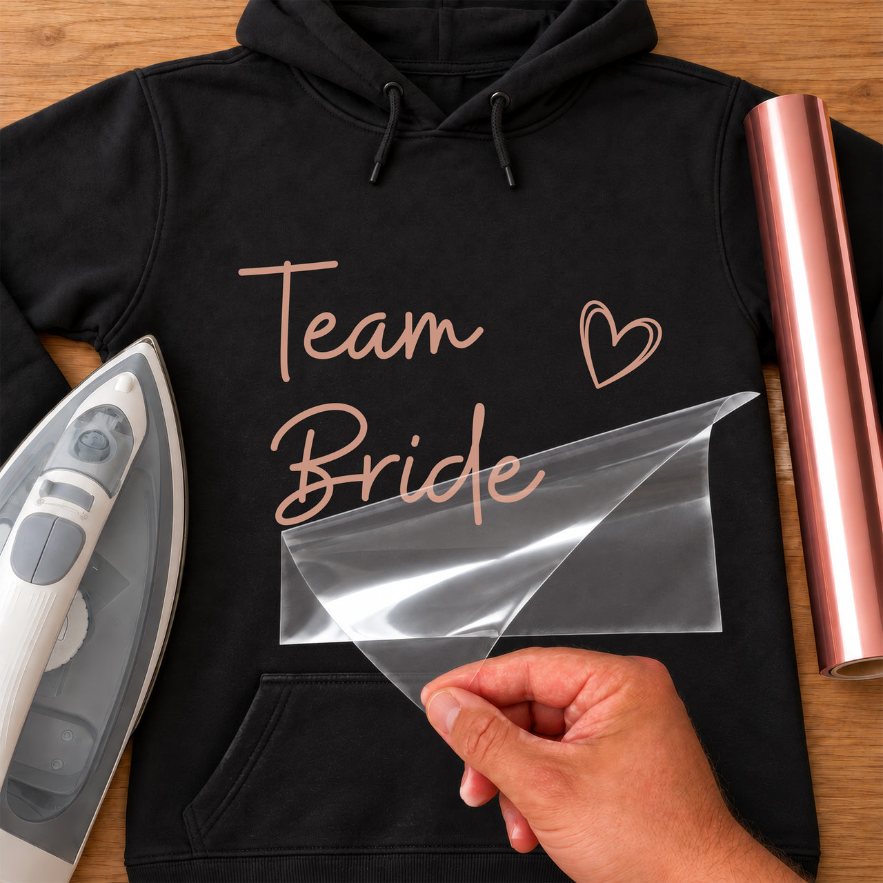 Black hoodie with rose gold script 'Team Bride' and a heart, hen party iron-on transfer being peeled