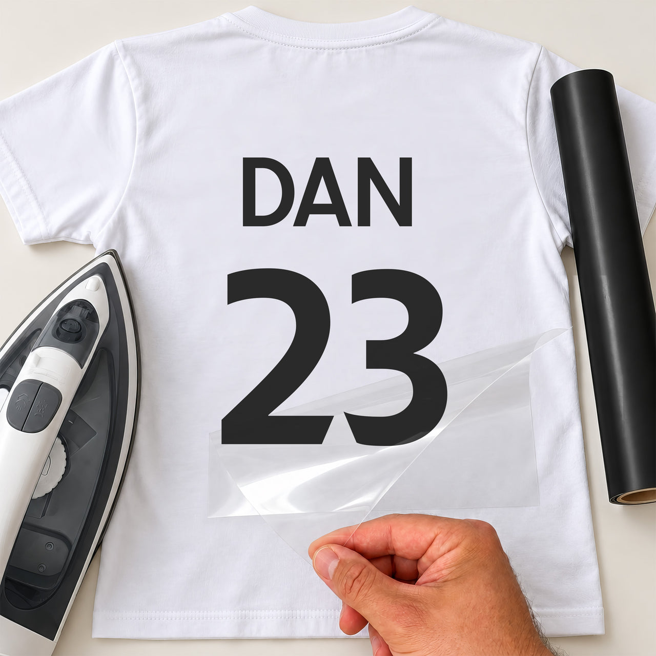 Team Building Shirt Name Number iron-on transfer: black DAN 23 on a white T-shirt, film being peeled