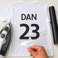 Team Building Shirt Name Number iron-on transfer: black DAN 23 on a white T-shirt, film being peeled