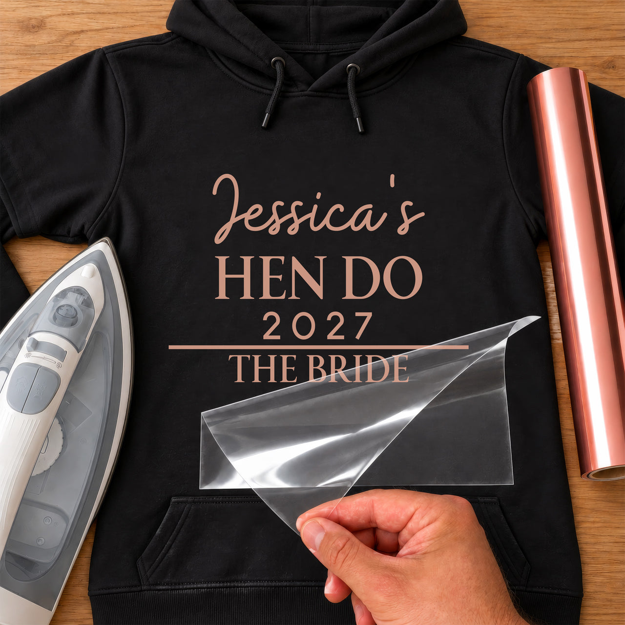 Black hoodie with rose gold 'Jessica's HEN DO 2027 THE BRIDE' iron-on transfer, iron and rose gold vinyl roll