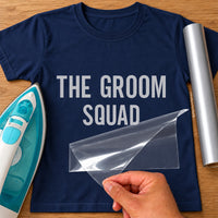 Navy T-shirt with silver 'THE GROOM SQUAD' iron-on transfer, clear carrier sheet lifted by hand next to an iron