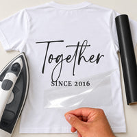 White T-shirt with black 'Together SINCE 2016' iron-on vinyl transfer, carrier sheet being peeled off, iron beside
