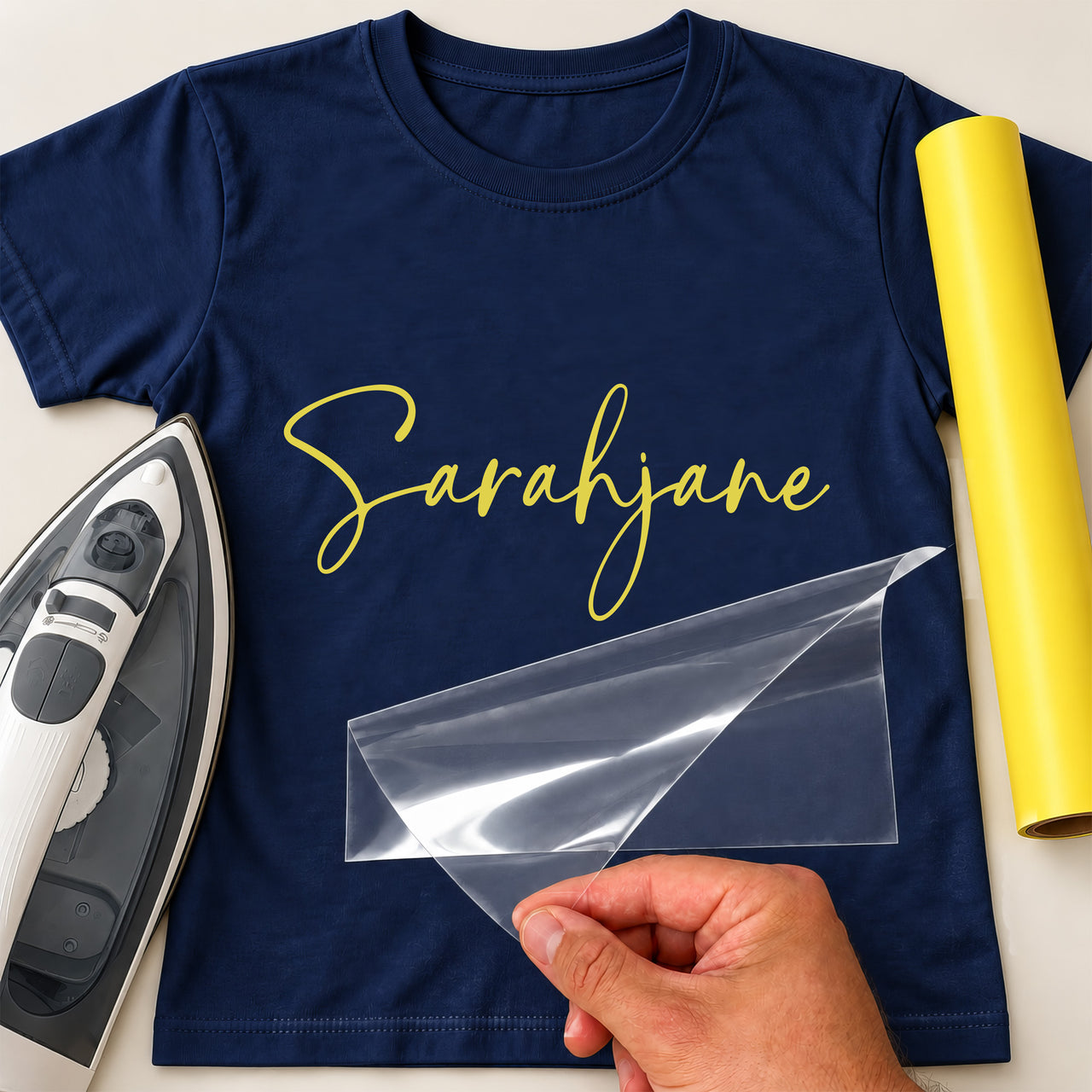 Unicorn Face iron-on transfer: yellow script Sarahjane on a navy T-shirt, film being peeled